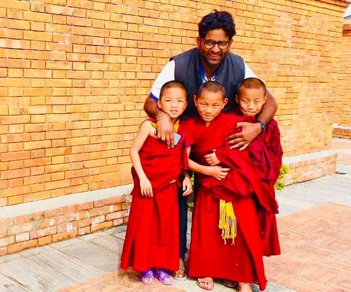 Dr. D.P. Shukla with three young monks in red robes beside a brick wall