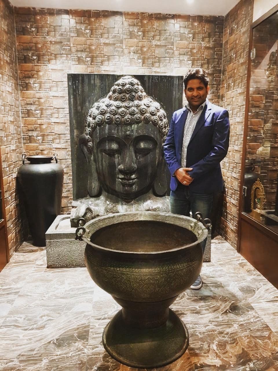 Dr. D.P. Shukla in a suit beside a large stone Buddha head