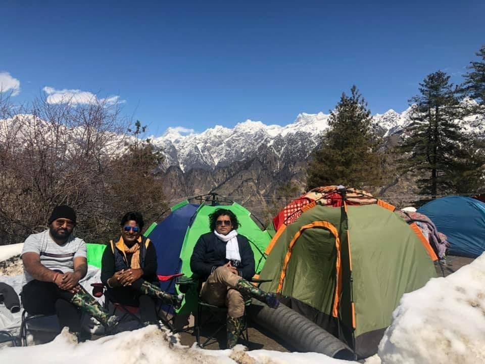 Friends beside tents pitched in deep snow below Himalayan peaks