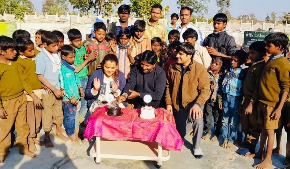 Dr. D.P. Shukla cutting a cake with a large group of children outdoors