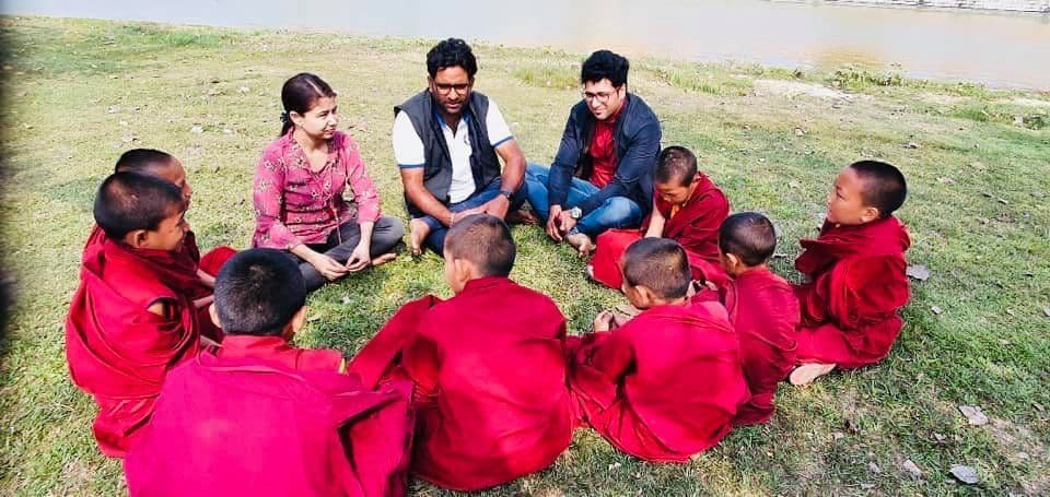 Dr. D.P. Shukla and companions sitting in a circle on the grass with young monks