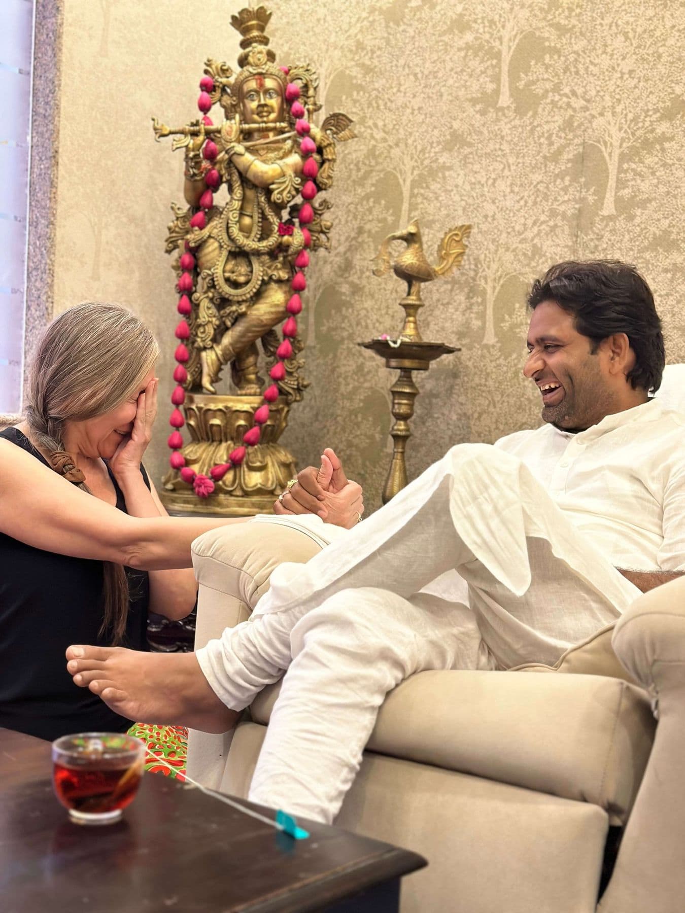 A visitor talks with Dr. D.P. Shukla beside a brass statue of Krishna and an oil lamp