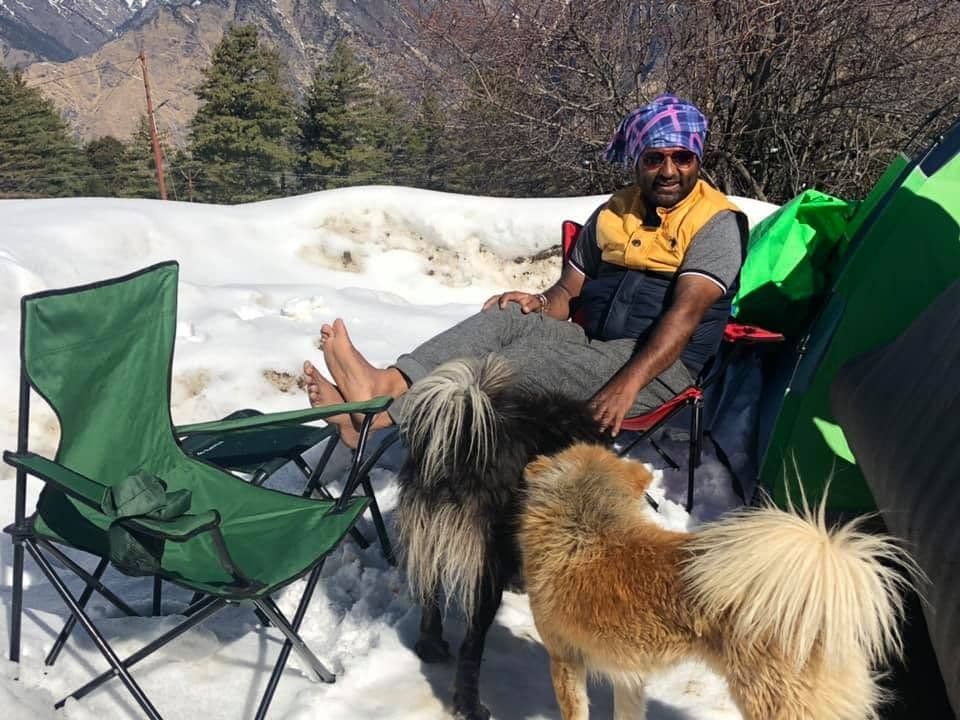 Dr. D.P. Shukla resting on a camp chair in the snow with two dogs