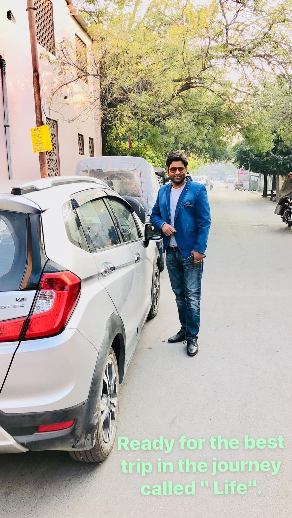Dr. D.P. Shukla beside a car on a tree-lined road, captioned “Ready for the best trip in the journey called life”