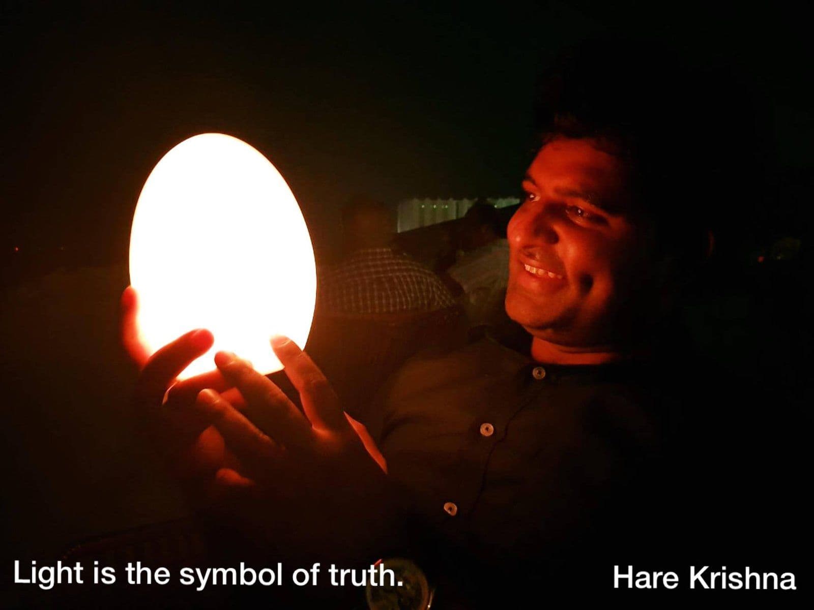 Dr. D.P. Shukla holding a glowing lamp, captioned “Light is the symbol of truth. Hare Krishna”