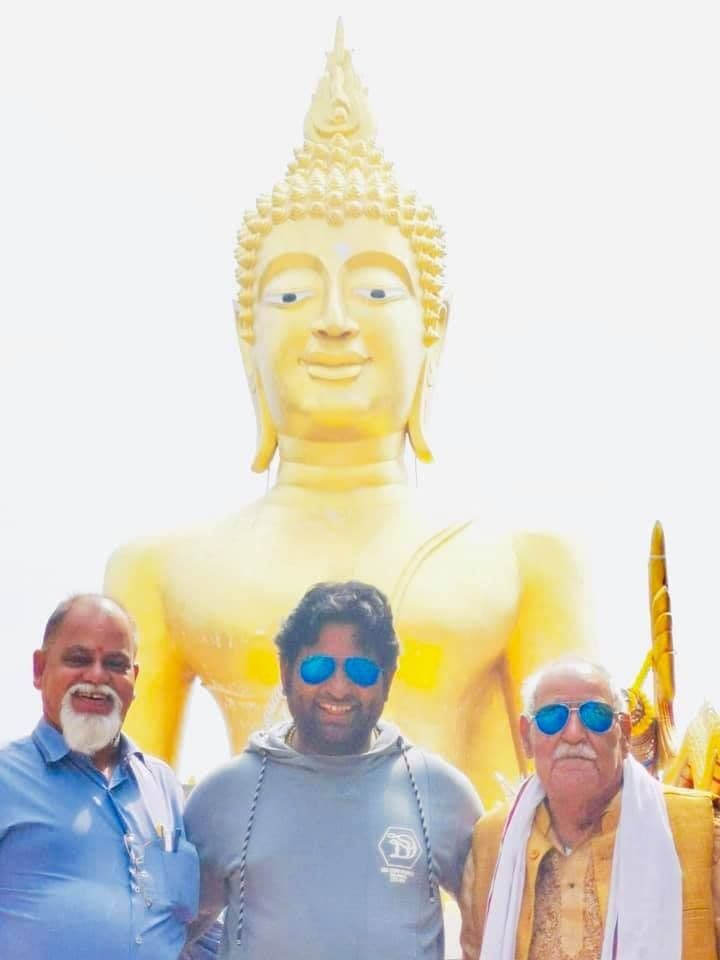 Dr. D.P. Shukla with two older men in front of a large golden Buddha statue