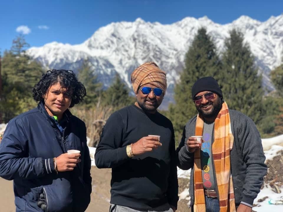 Dr. D.P. Shukla with two friends holding cups of tea in the snow, mountains behind