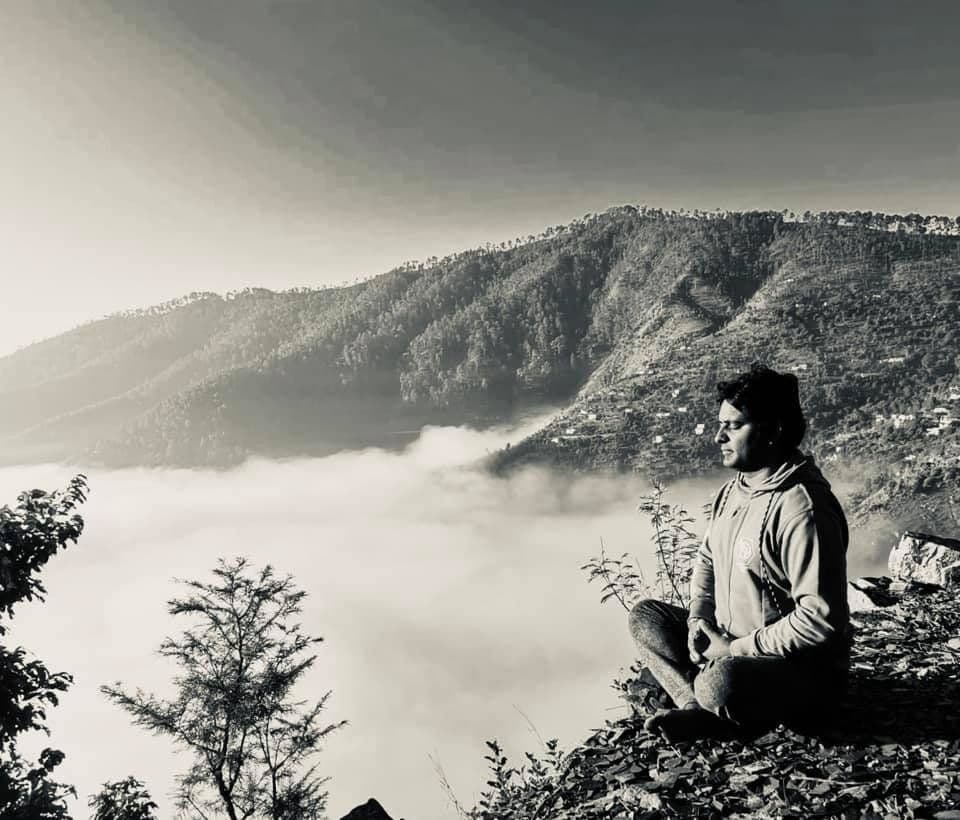 Black-and-white photo of Dr. D.P. Shukla seated on a hilltop above the clouds