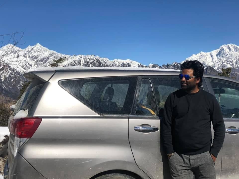 Dr. D.P. Shukla beside a car on a mountain road below snowy peaks