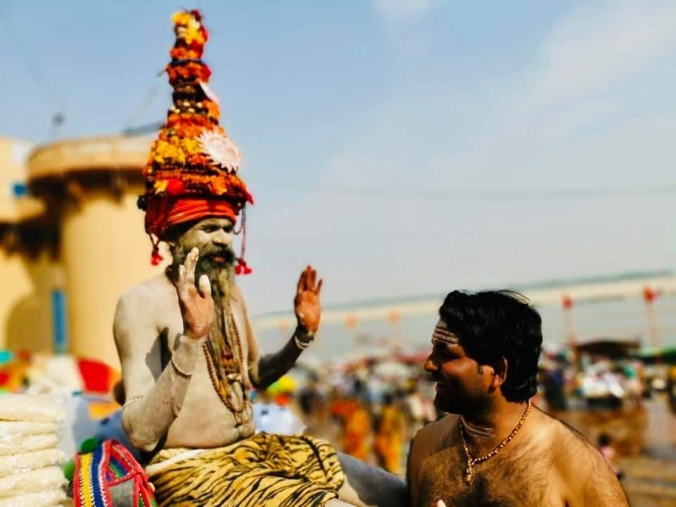 Dr. D.P. Shukla with a sadhu in an orange turban at a riverside ghat, both raising a hand