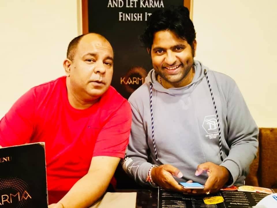 Dr. D.P. Shukla with a friend under a sign reading “And let karma finish!”