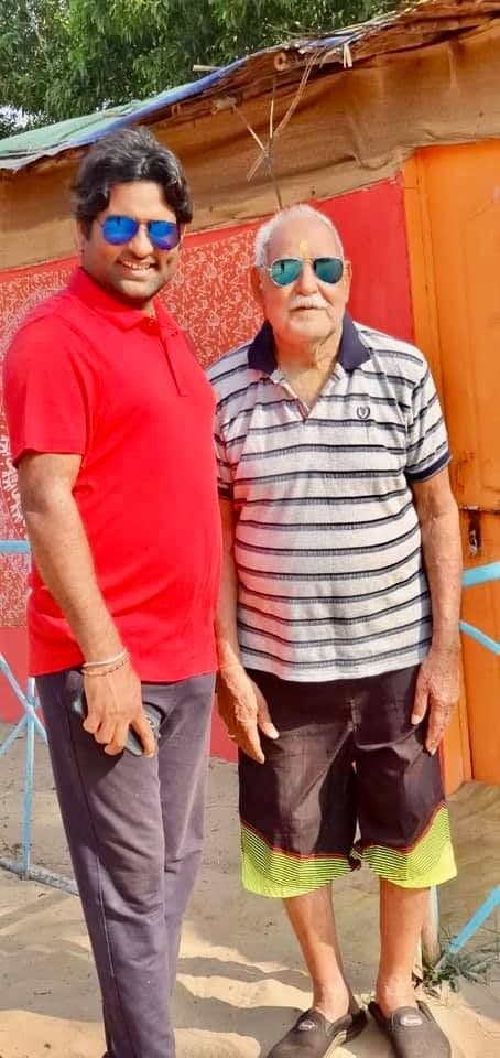 Dr. D.P. Shukla in a red shirt standing beside an older man outdoors