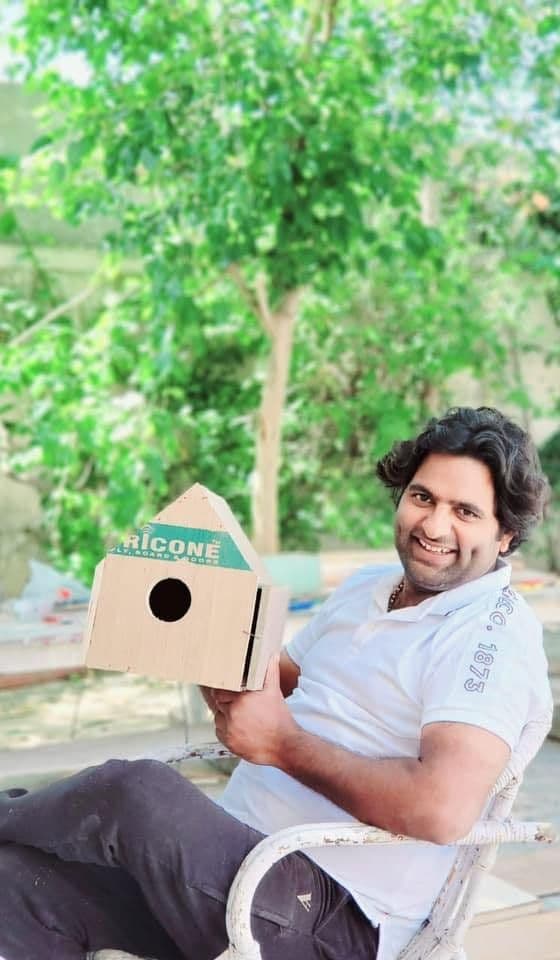 Dr. D.P. Shukla sitting outdoors holding a wooden birdhouse