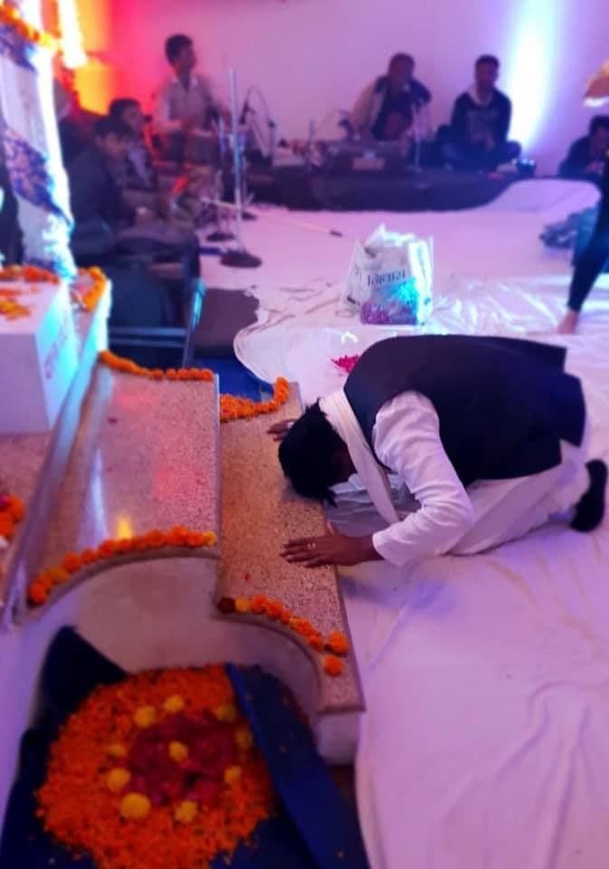 A devotee bowing before a flower rangoli at an evening gathering